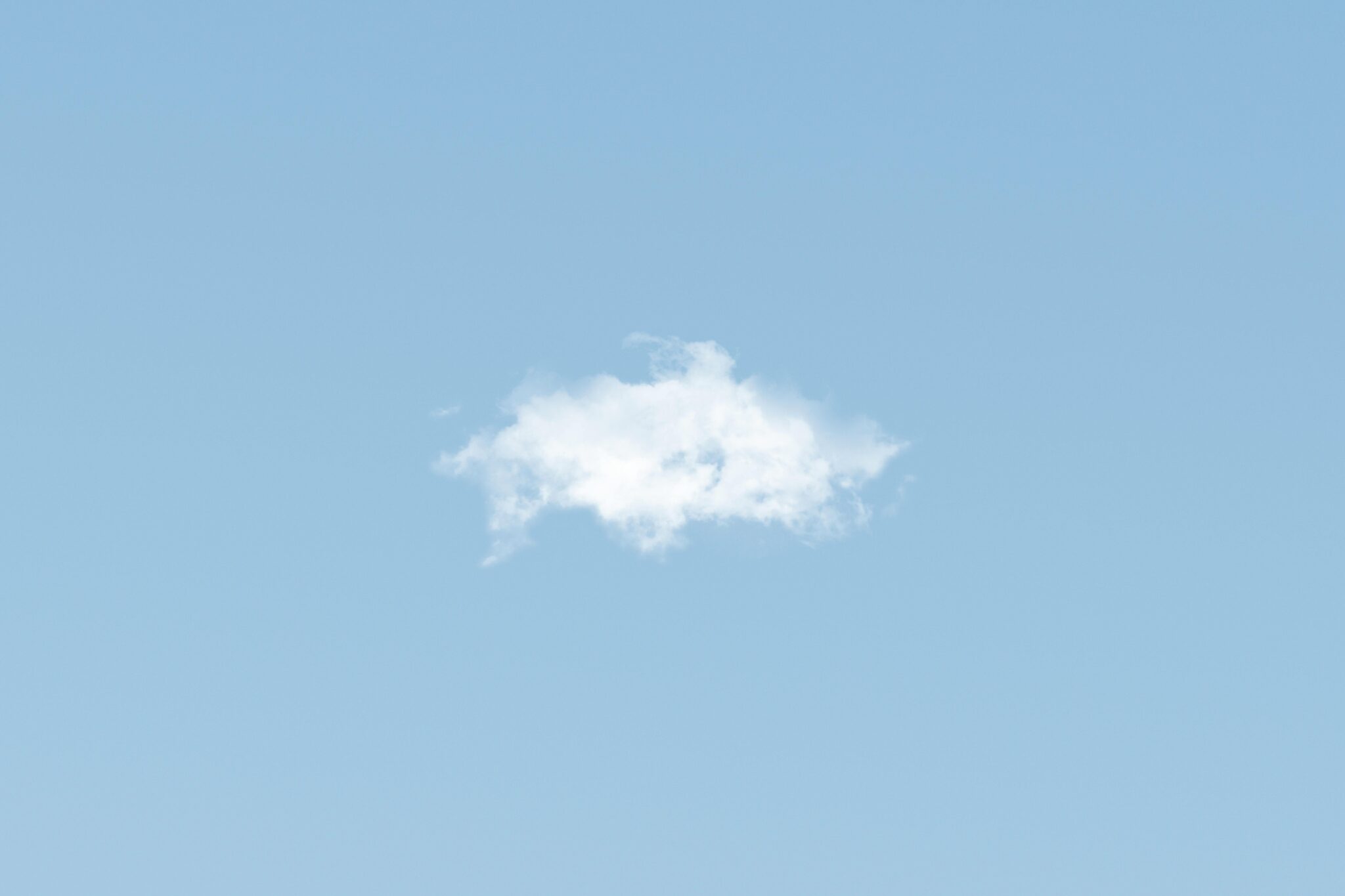 A lone white cloud floats peacefully in a clear blue sky, ideal for backgrounds.